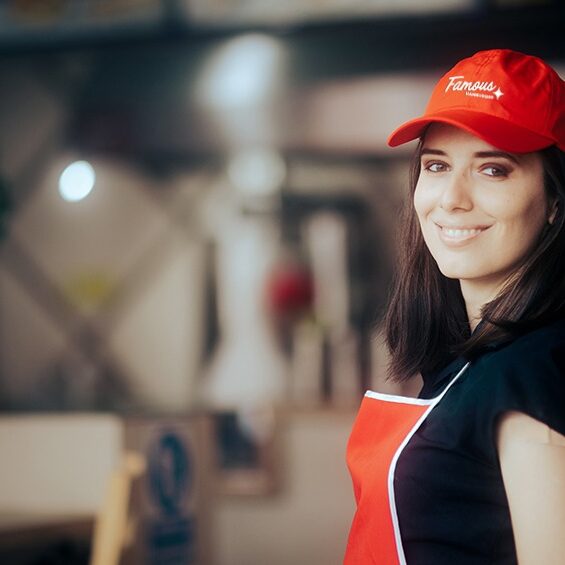Smiling team member in a red Famous Hamburger branded uniform cap and apron